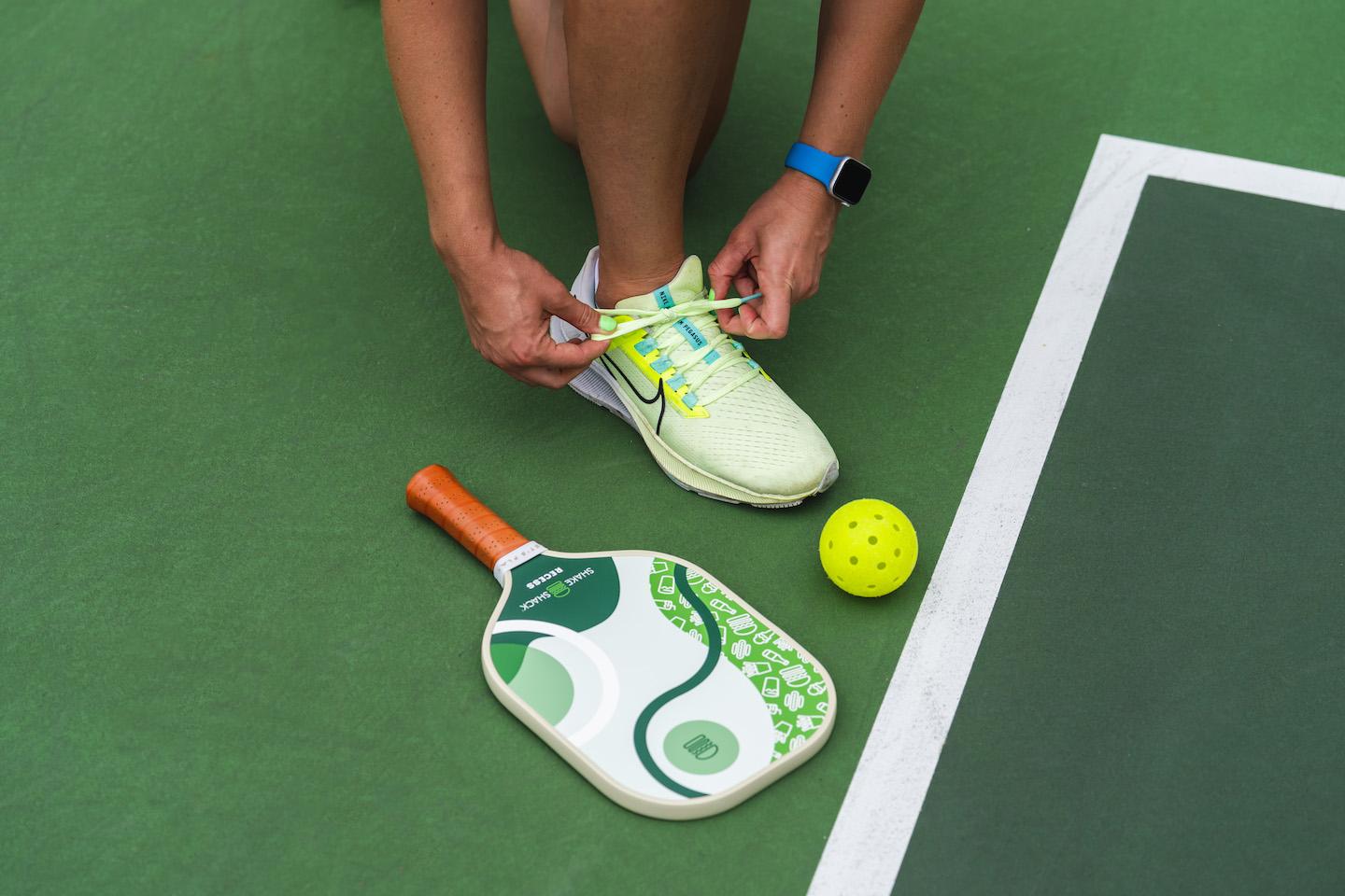 Pickleball athlete tying shoe in court