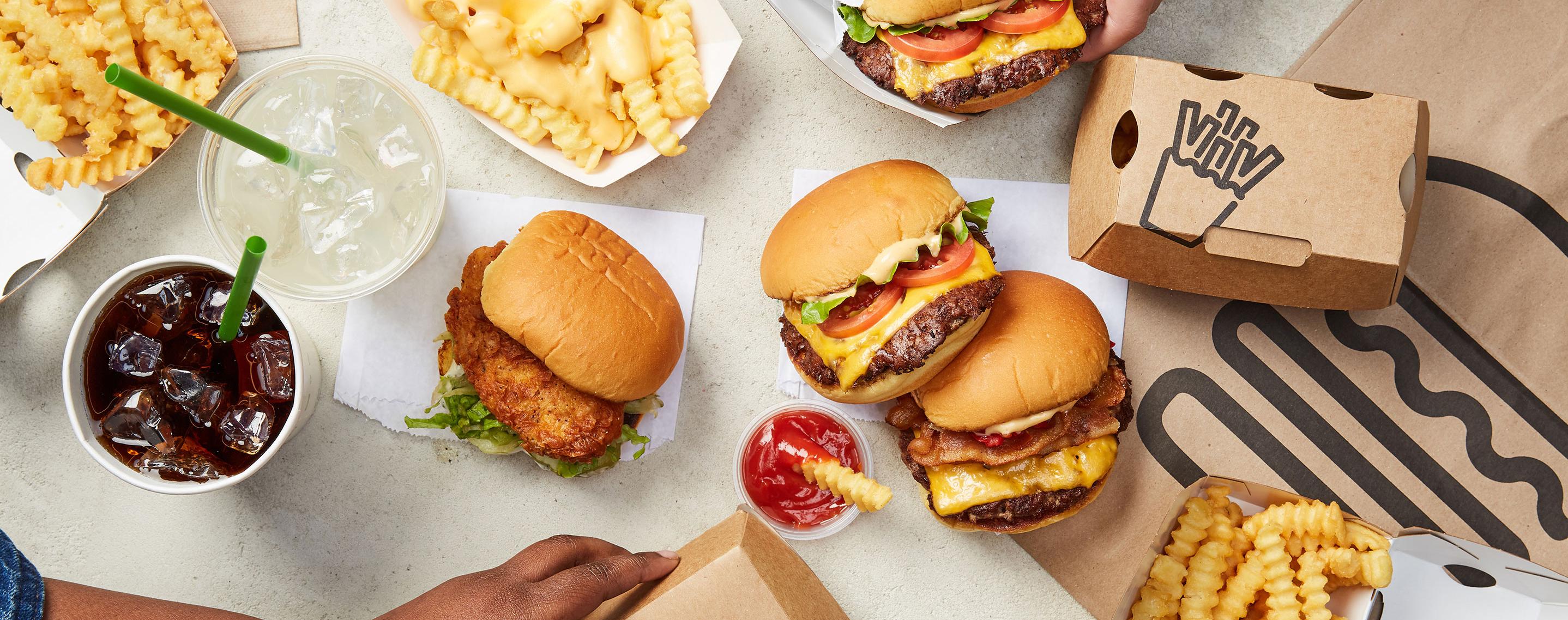 Group of burgers, fries and drinks, People reaching into frame